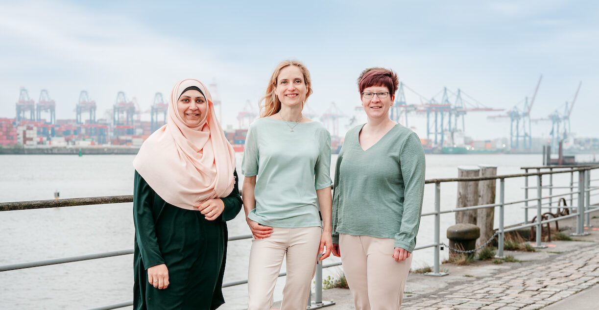 Drei-Frauen-Team von PrioService an der Elbe mit dem Hamburger Hafen im Hintergrund