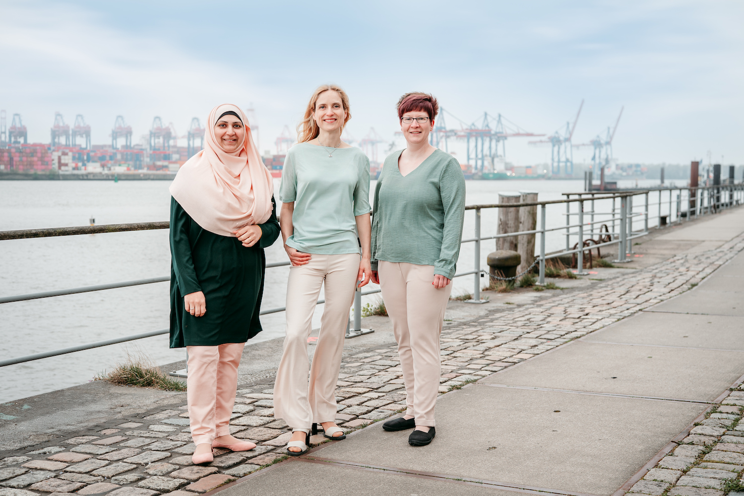 Drei-Frauen-Team von PrioService an der Elbe mit dem Hamburger Hafen im Hintergrund